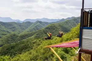 Two people riding a zipline over lush green mountains
